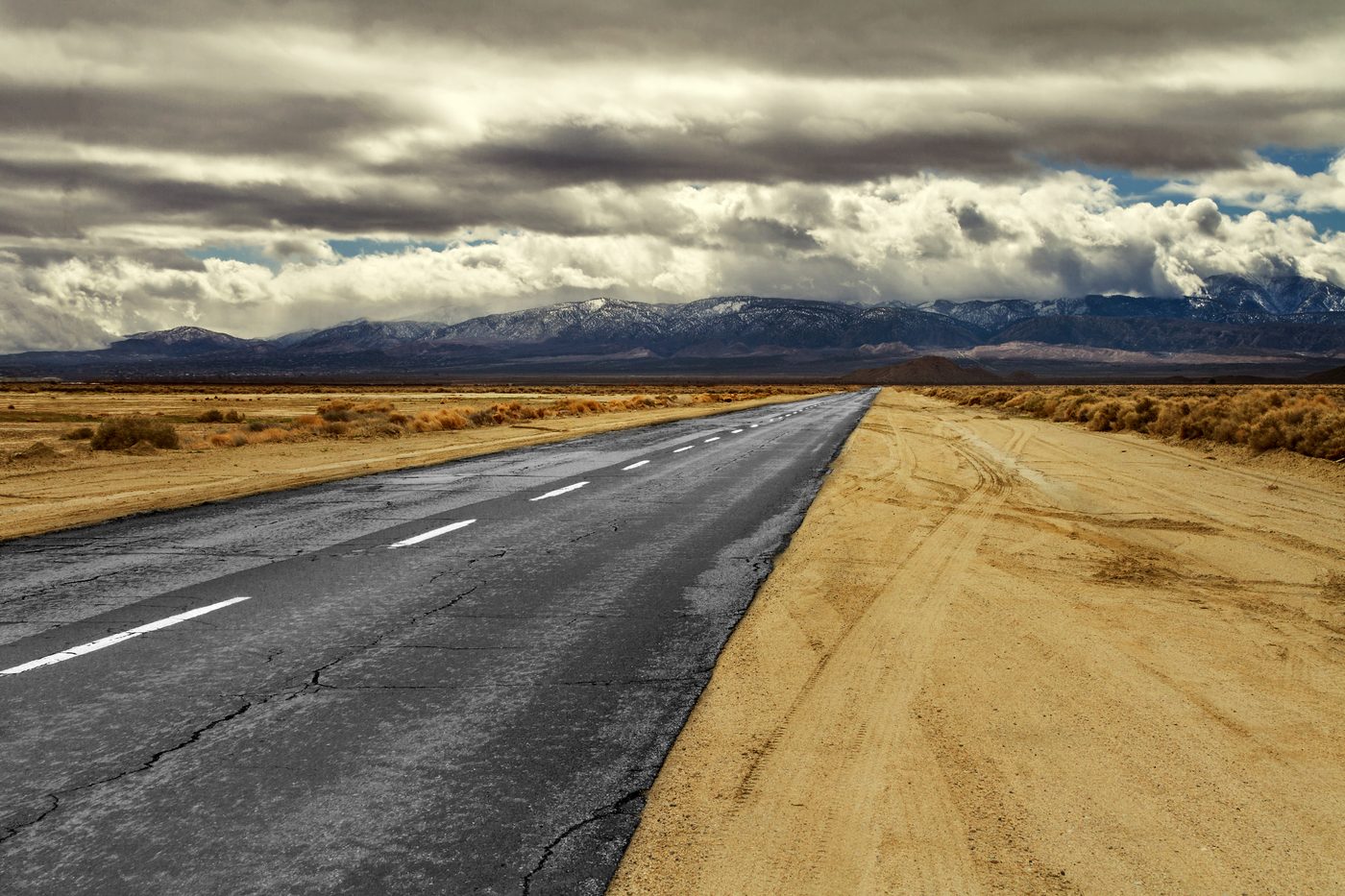 An open two-lane desert highway running toward distant mountains under a big cloudy Nevada sky